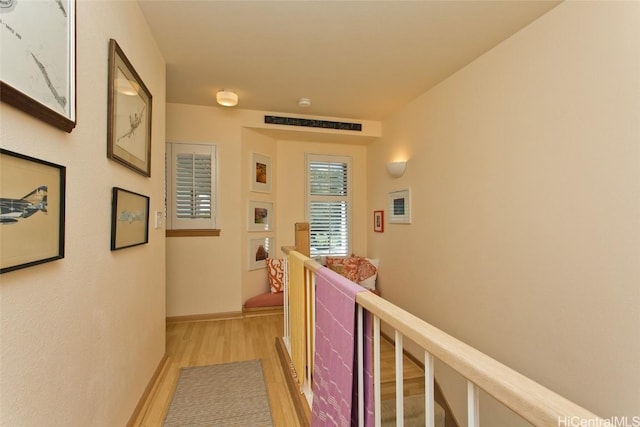 corridor featuring light wood finished floors, an upstairs landing, and baseboards