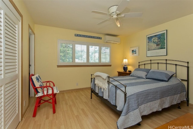 bedroom with a wall unit AC, a ceiling fan, baseboards, and wood finished floors