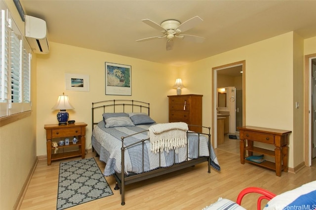 bedroom with ensuite bathroom, light wood finished floors, a wall mounted air conditioner, and baseboards