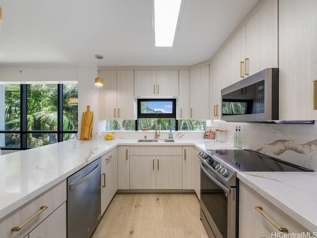 kitchen featuring a skylight, a sink, appliances with stainless steel finishes, light stone countertops, and pendant lighting