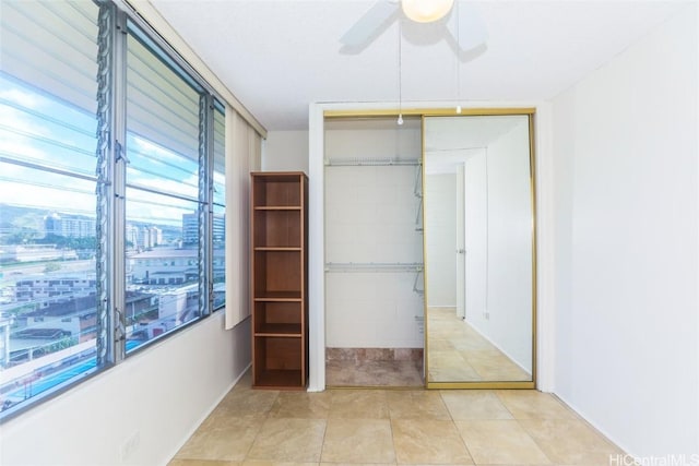 unfurnished bedroom with a closet, light tile patterned floors, a city view, and a ceiling fan