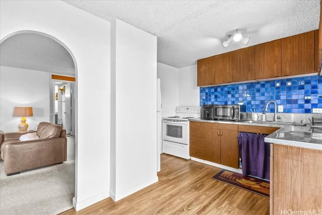 kitchen with arched walkways, light countertops, light wood-style floors, stainless steel microwave, and white electric range