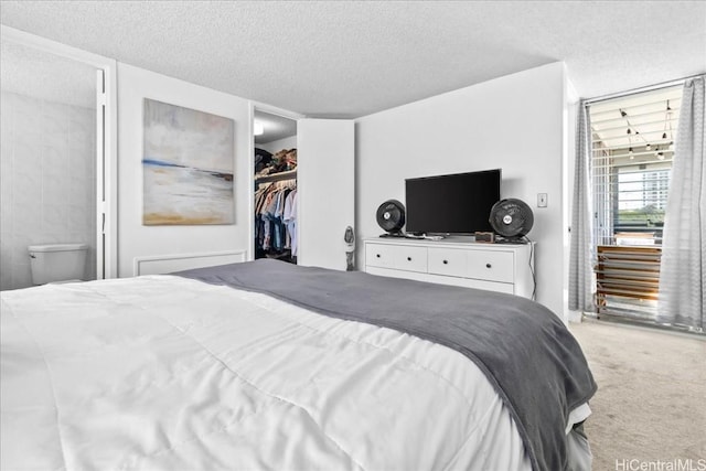 carpeted bedroom featuring a spacious closet, a textured ceiling, and ensuite bath