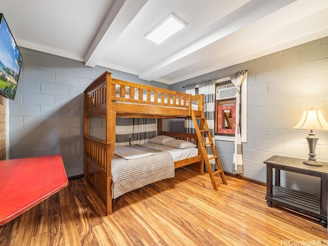 bedroom featuring beamed ceiling, wood finished floors, and concrete block wall