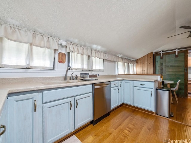 kitchen featuring white cabinets, light countertops, stainless steel dishwasher, light wood-style floors, and a sink