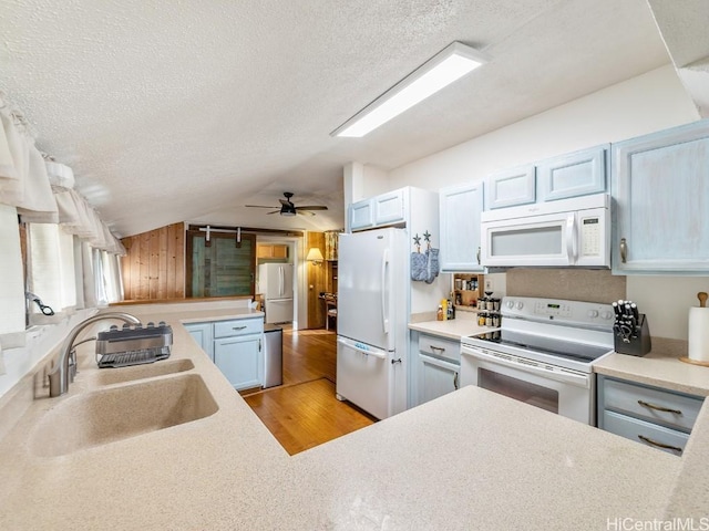 kitchen featuring lofted ceiling, a textured ceiling, white appliances, a sink, and light countertops