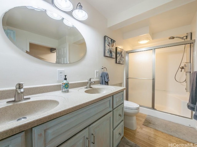 full bath featuring double vanity, a sink, a shower stall, and wood finished floors