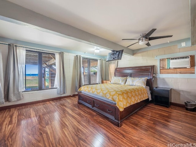 bedroom with dark wood-style floors, concrete block wall, a wall mounted air conditioner, and a ceiling fan