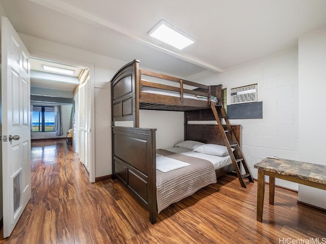 bedroom featuring a wall unit AC, wood finished floors, and concrete block wall