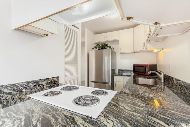 kitchen featuring cooktop, white cabinets, dark stone countertops, freestanding refrigerator, and a sink