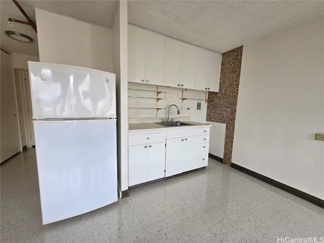 kitchen with a textured ceiling, white cabinetry, freestanding refrigerator, and a sink