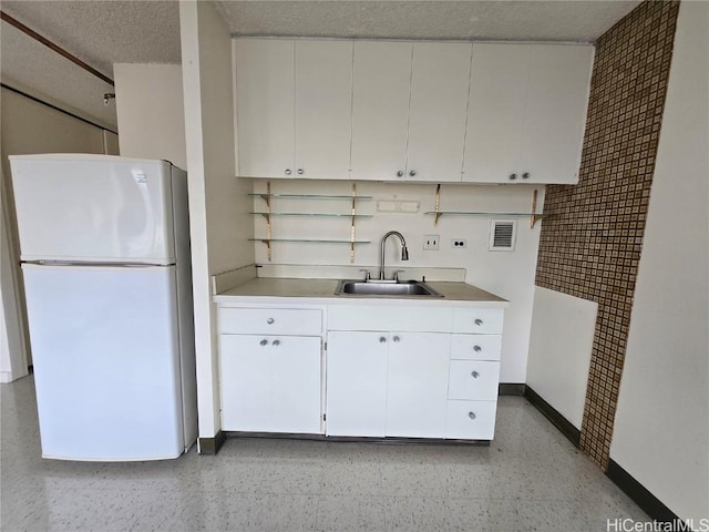 kitchen featuring freestanding refrigerator, white cabinets, a textured ceiling, light speckled floor, and a sink