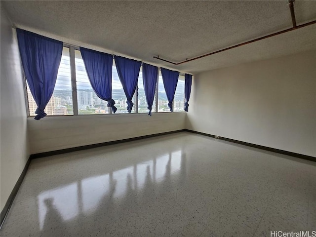 spare room featuring speckled floor, baseboards, and a textured ceiling