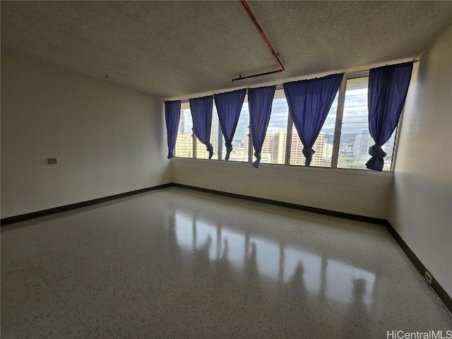 empty room with speckled floor, baseboards, a textured ceiling, and a healthy amount of sunlight