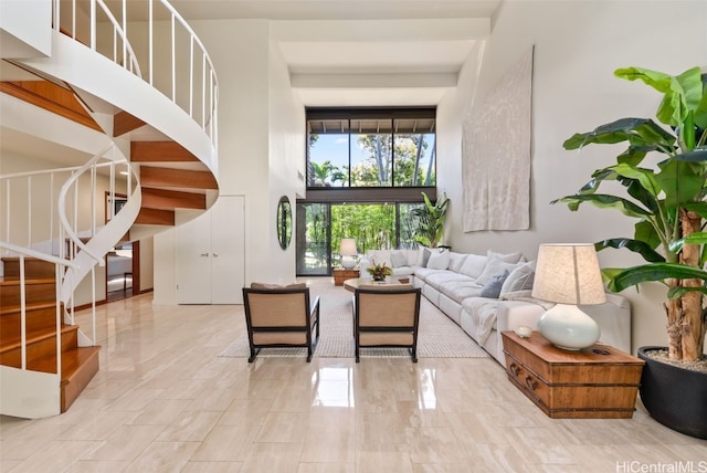 living area with beam ceiling, a high ceiling, and stairs