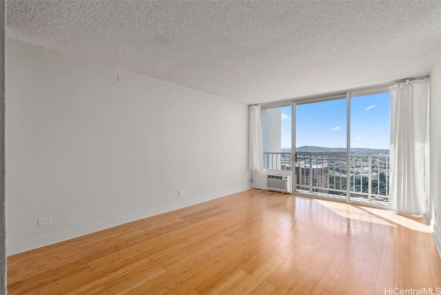 unfurnished room featuring baseboards, wood finished floors, a wall mounted air conditioner, expansive windows, and a textured ceiling