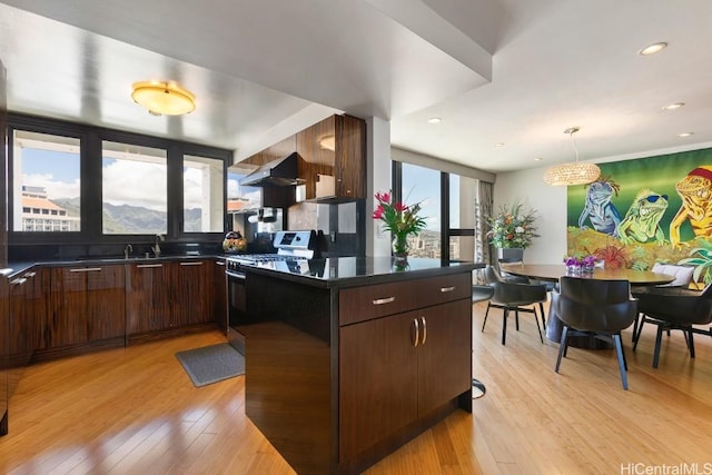 kitchen with dark brown cabinetry, under cabinet range hood, stainless steel range with gas cooktop, dark countertops, and pendant lighting