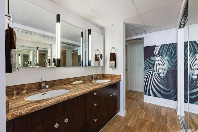 bathroom featuring double vanity, a paneled ceiling, a sink, and wood finished floors