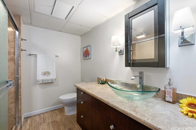 full bath with baseboards, toilet, wood finished floors, vanity, and a paneled ceiling