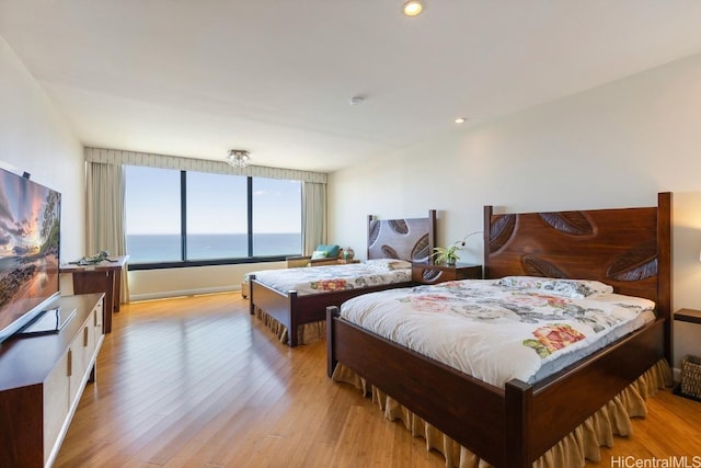 bedroom with light wood-type flooring, a water view, and recessed lighting