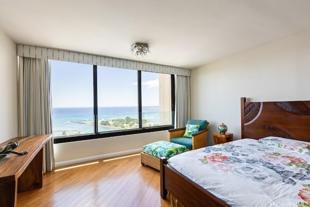 bedroom with a water view, light wood-style flooring, and baseboards