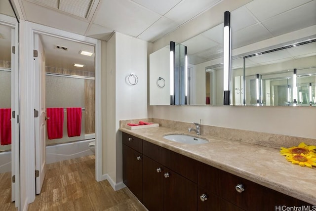 full bath featuring a paneled ceiling, toilet, shower / bath combination with glass door, visible vents, and vanity