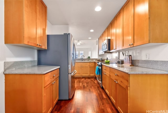 kitchen featuring a ceiling fan, a sink, light stone counters, dark wood finished floors, and appliances with stainless steel finishes