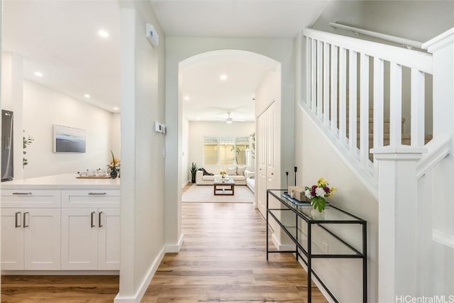 hallway with arched walkways, light wood-type flooring, baseboards, and recessed lighting