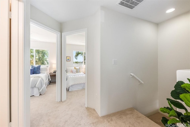 hall featuring light carpet, an upstairs landing, and visible vents