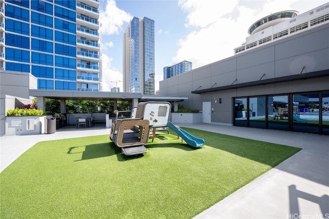 community jungle gym with a yard, a patio, and a city view