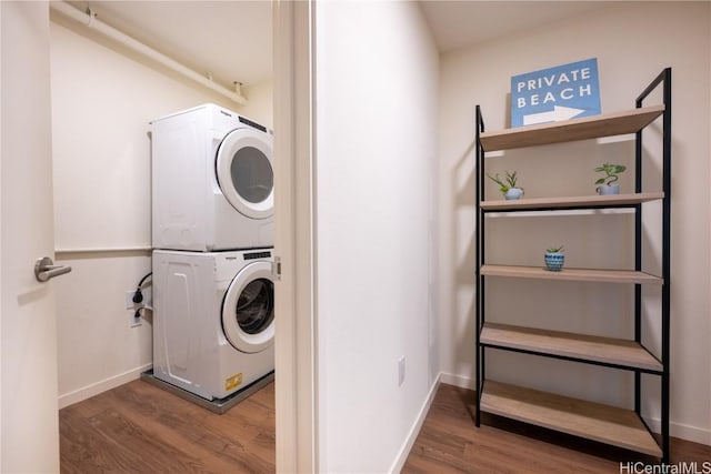 laundry room with laundry area, stacked washer and dryer, wood finished floors, and baseboards