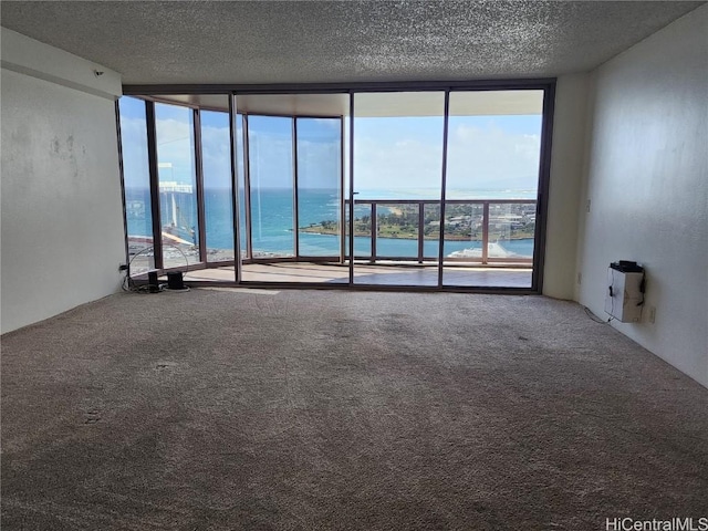 carpeted spare room with a water view, floor to ceiling windows, and a textured ceiling