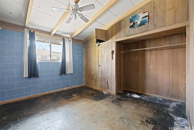 unfurnished bedroom with concrete block wall, a closet, wood walls, concrete floors, and beam ceiling