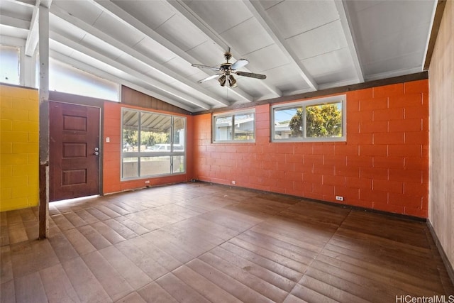 spare room with a ceiling fan, a wealth of natural light, vaulted ceiling with beams, and concrete block wall