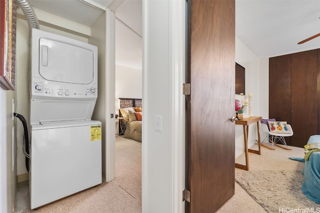 clothes washing area featuring laundry area, light colored carpet, and stacked washer and clothes dryer