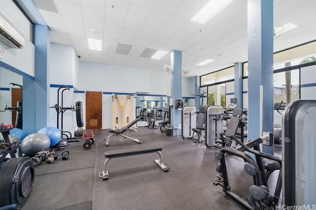 gym featuring a wall unit AC, a towering ceiling, and a drop ceiling