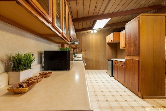 kitchen featuring light floors, wood walls, light countertops, and beam ceiling