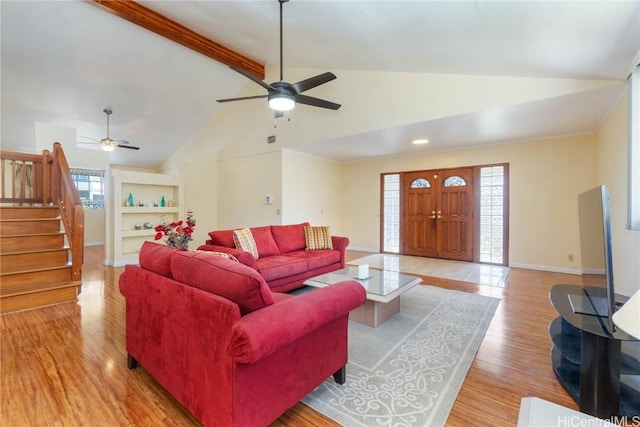 living area featuring stairway, beamed ceiling, light wood-style flooring, and built in shelves