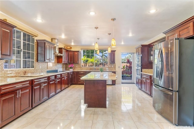 kitchen with a center island, hanging light fixtures, appliances with stainless steel finishes, wall chimney range hood, and decorative backsplash