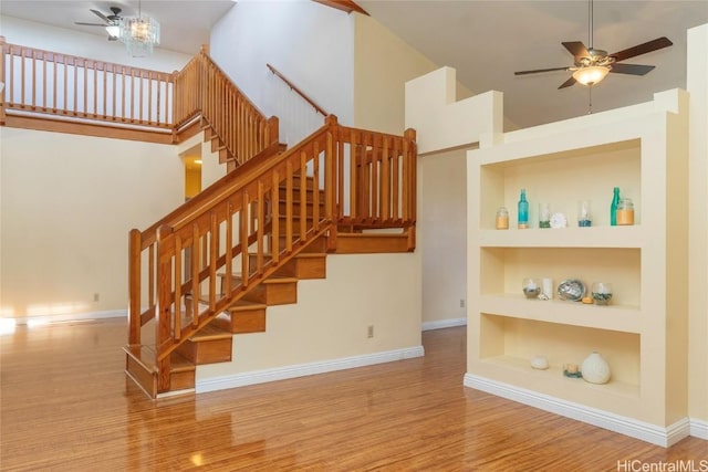 staircase featuring baseboards, built in features, a towering ceiling, ceiling fan, and wood finished floors