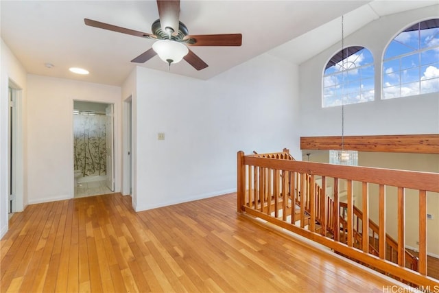 hallway featuring lofted ceiling, light wood-style flooring, an upstairs landing, and baseboards