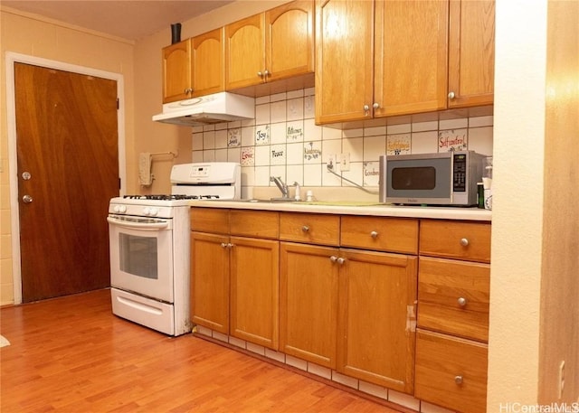 kitchen featuring under cabinet range hood, light countertops, light wood-type flooring, white gas range oven, and stainless steel microwave