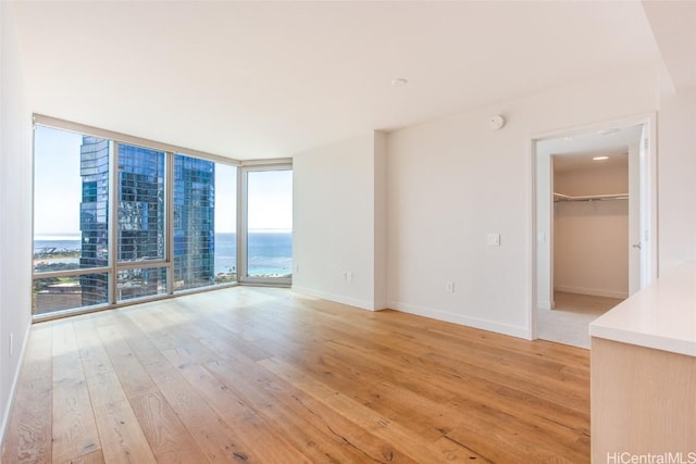 empty room with baseboards, light wood-style floors, a water view, and floor to ceiling windows