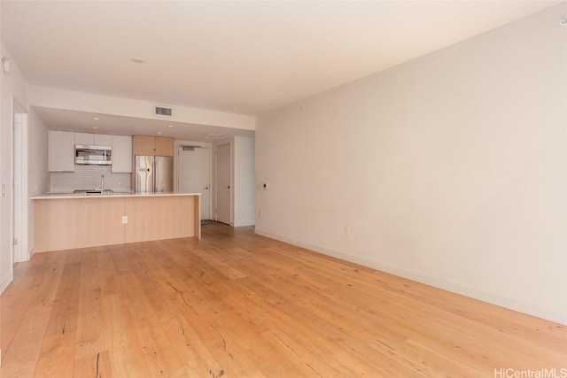 unfurnished living room with light wood-type flooring, a sink, visible vents, and baseboards