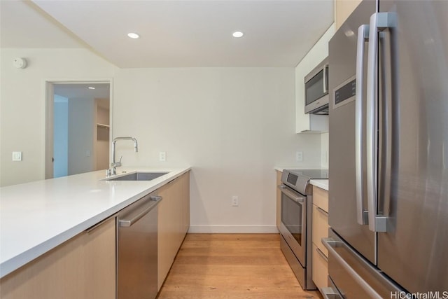 kitchen with light wood-style flooring, stainless steel appliances, a sink, and light countertops