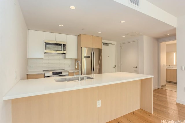 kitchen with light wood finished floors, stainless steel appliances, light countertops, visible vents, and backsplash