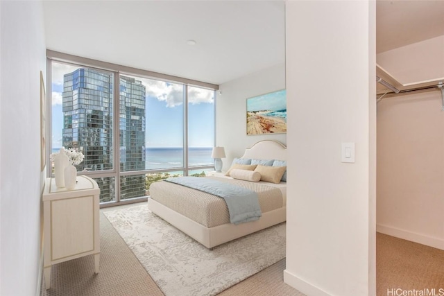 bedroom with a water view, baseboards, a wall of windows, and carpet flooring