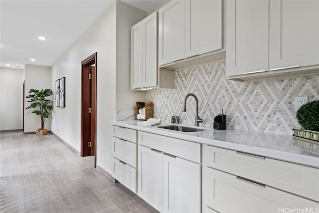 kitchen featuring tasteful backsplash, white cabinets, light stone counters, light wood-type flooring, and a sink