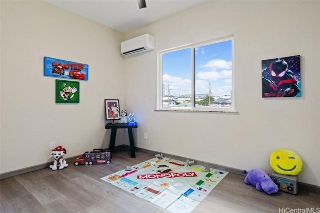 game room with a wall mounted air conditioner, wood finished floors, and baseboards