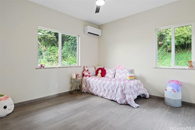 bedroom featuring a ceiling fan, a wall mounted air conditioner, baseboards, and wood finished floors